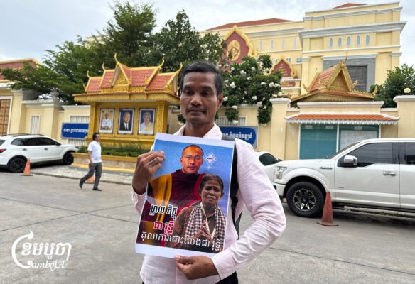 An activist holds a portrait of defrocked monk Chea Vuthy outside the Phnom Penh Municipal Court after he was sentenced to 18 months in prison. Aug. 19, 2026. (CamboJA/Try Thaney)